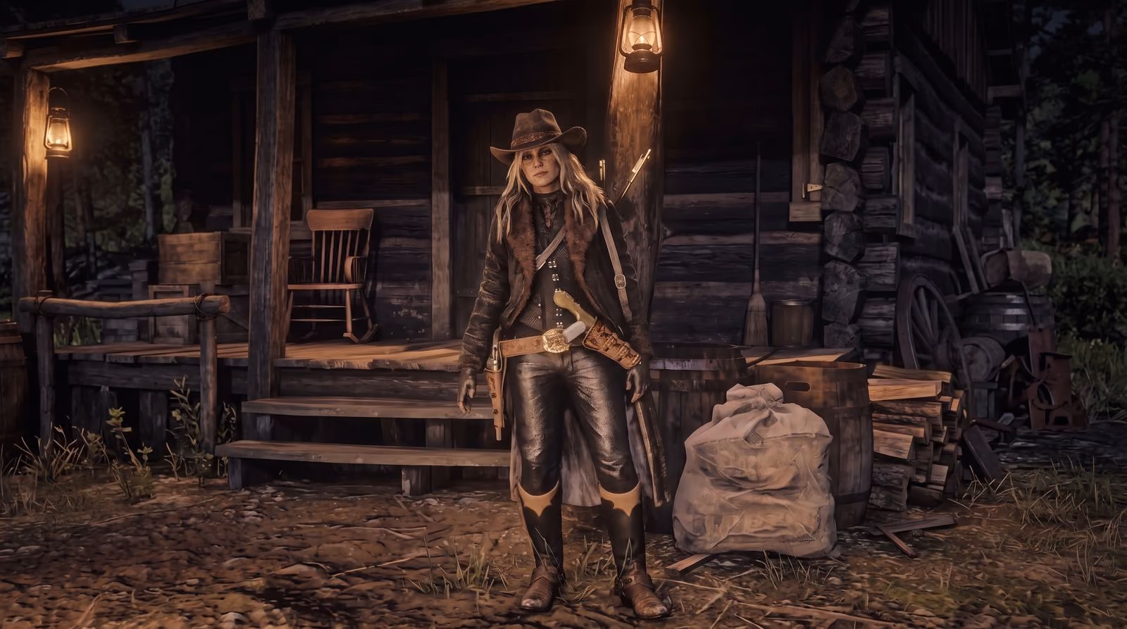 A woman in a long coat and hat stands in front of a log cabin porch at dusk, two lanterns lit either side of the door, sacks and firewood at her feet.