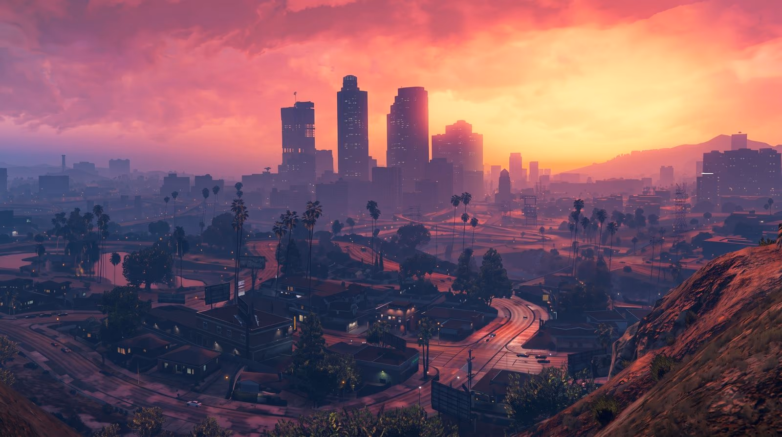 The city from the hills at dusk: a low skyline under a pink and orange sky, streetlights coming on across the flats below.