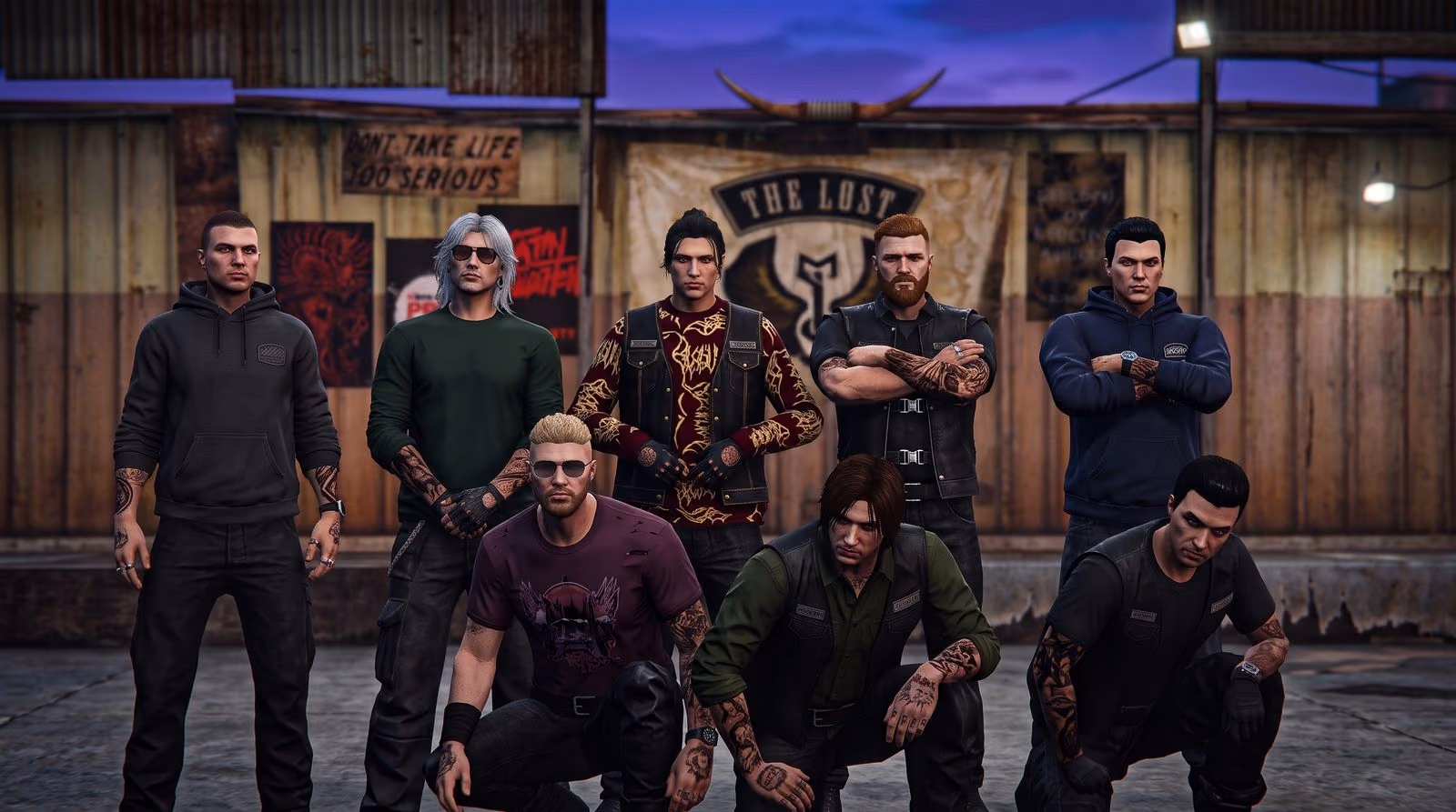 Nine men in dark jackets pose in two rows at night in front of a corrugated clubhouse wall hung with signs, lit from the front.