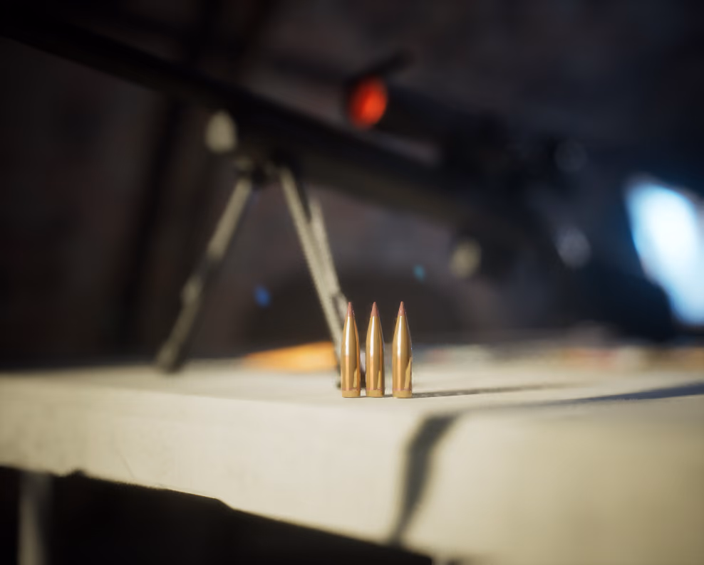 Three brass rounds standing sharp on the edge of the table with the rifle and its lit scope thrown out of focus above them, the tent almost black, a screen glowing blue at the right edge.